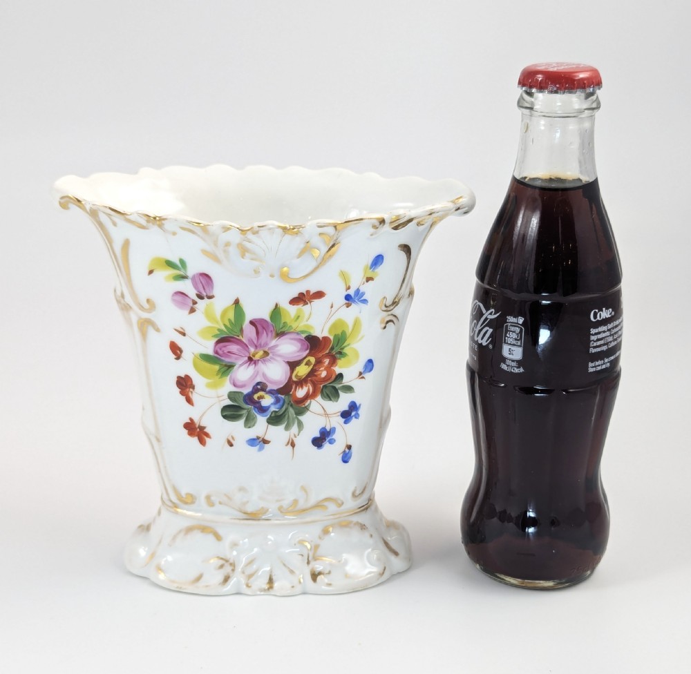 A white hard-paste porcelain vase featuring a flared scalloped rim, hand-painted floral display, and gilded Rococo scroll accents. View IX