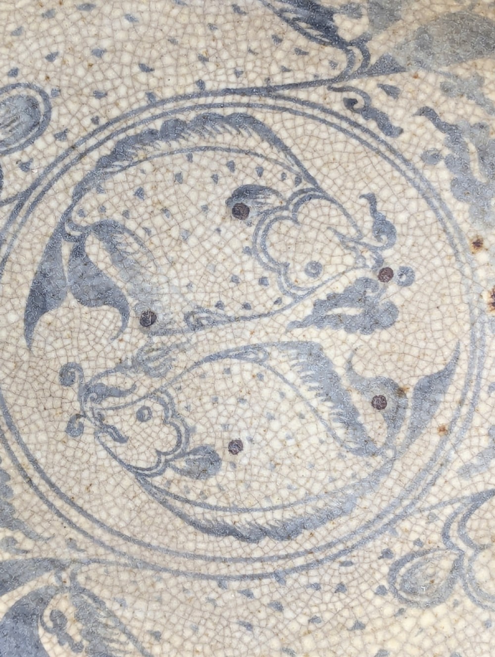 A circular antique ceramic dish featuring a central underglaze grey fish design on a crazed cream ground. View II