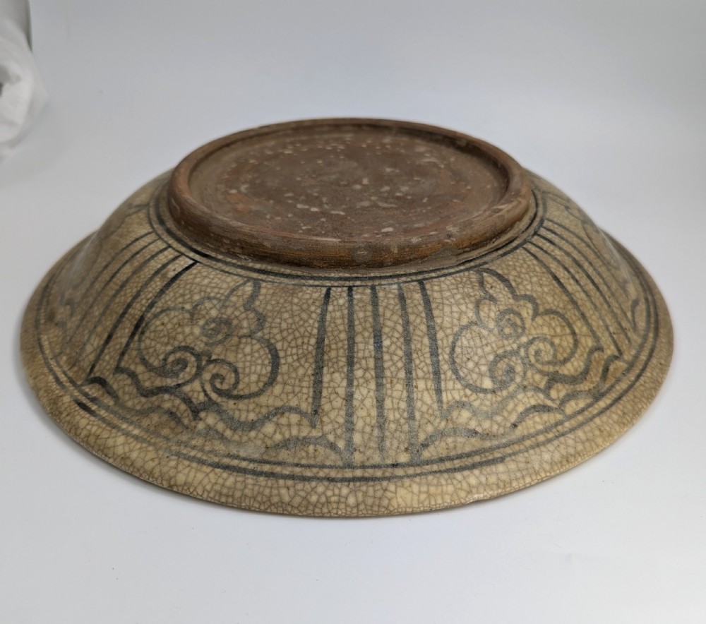A circular antique ceramic dish featuring a central underglaze grey fish design on a crazed cream ground. View VI