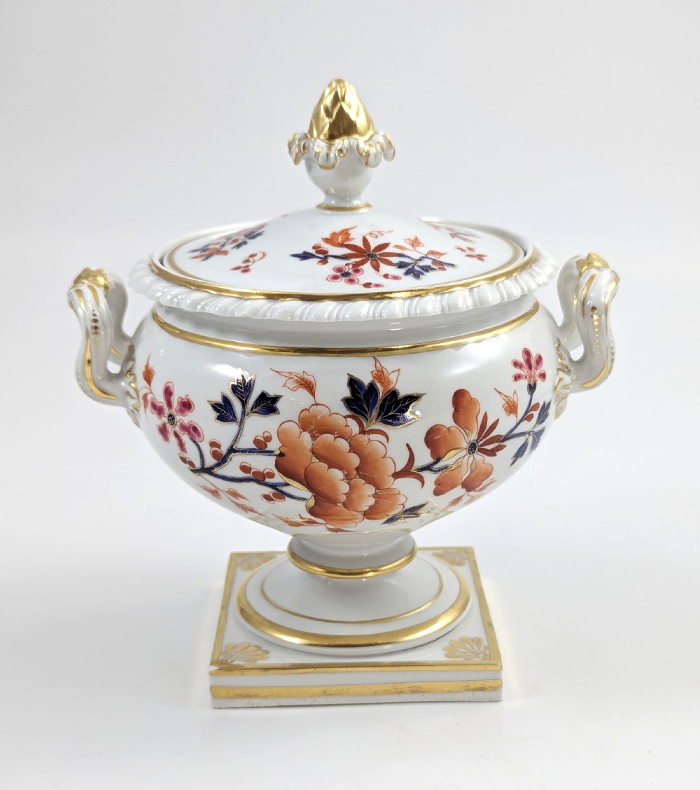 A white Regency porcelain sauce tureen decorated with orange and blue floral Imari motifs, featuring twin gilded handles, a square pedestal base, and a domed lid with a gilded finial. View IV