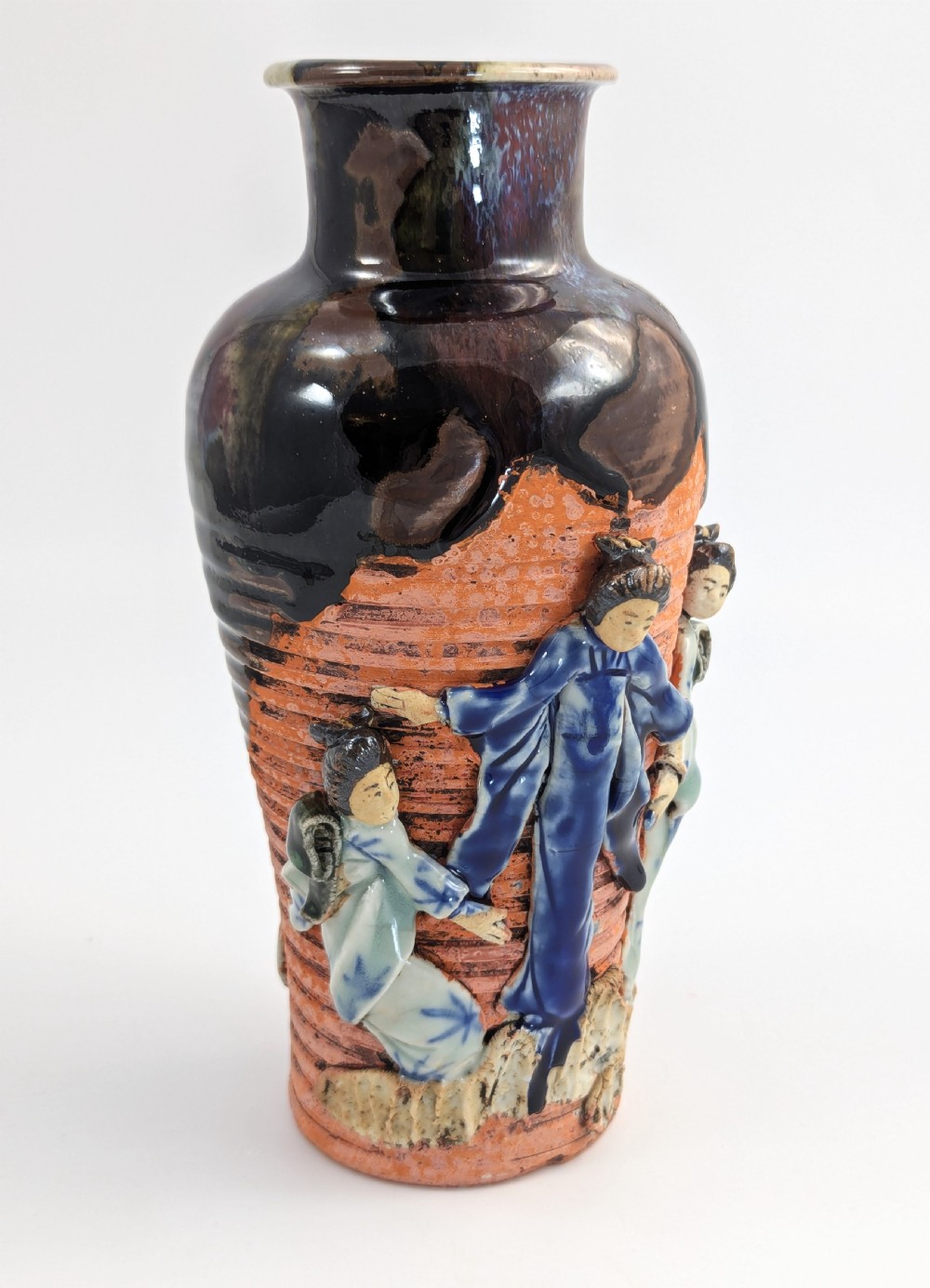 A Japanese Sumida Gawa pottery vase featuring an oxblood flambe glazed neck and applied relief figures on a ribbed terracotta body. View VI
