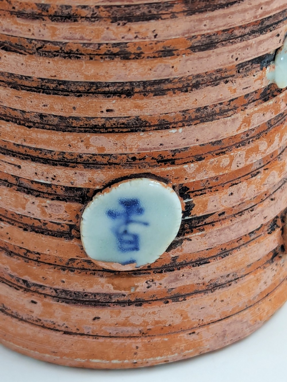 A Japanese Sumida Gawa pottery vase featuring an oxblood flambe glazed neck and applied relief figures on a ribbed terracotta body. View IX