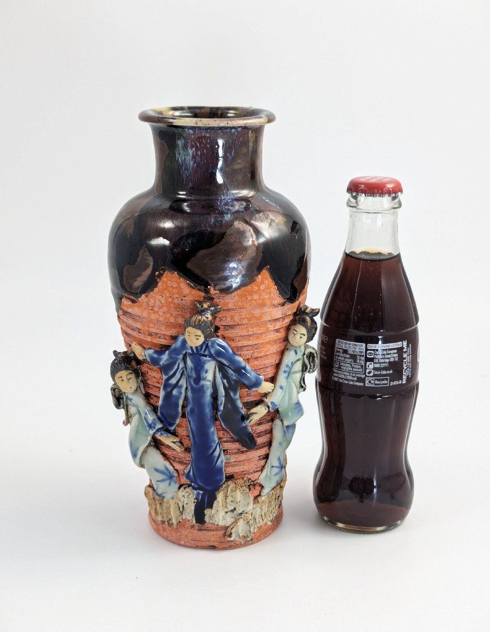 A Japanese Sumida Gawa pottery vase featuring an oxblood flambe glazed neck and applied relief figures on a ribbed terracotta body. View X