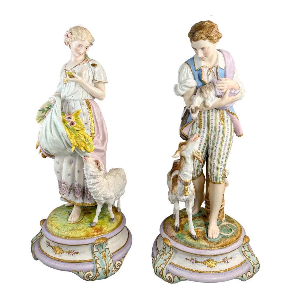 A pair of large French bisque porcelain sculptures featuring a shepherd and shepherdess with animals on gilded bases.