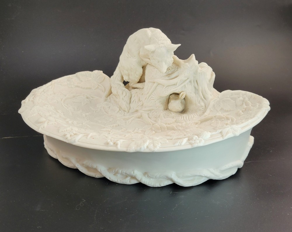 An off-white Parian porcelain centrepiece dish featuring a sculpted fox perched on a central stump above a rabbit in a hollow base surrounded by leaves. View II
