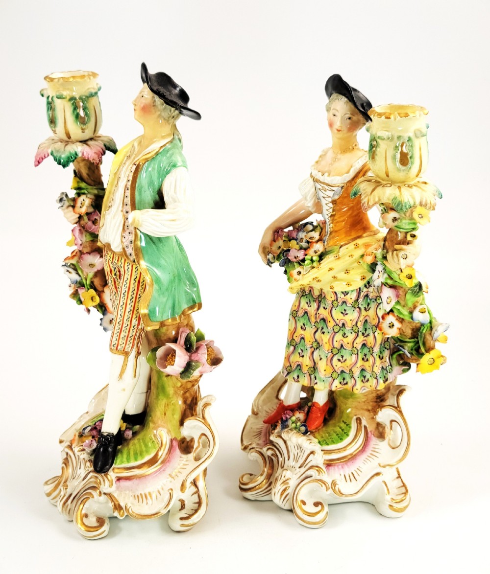 A pair of 18th-century Georgian Derby soft-paste porcelain figural candlesticks depicting a male and female figure in period dress beside candle sconces adorned with colourful flowers and gilt Rococo scrollwork. View II
