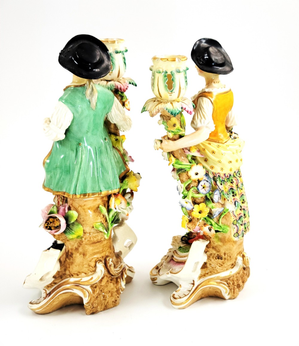 A pair of 18th-century Georgian Derby soft-paste porcelain figural candlesticks depicting a male and female figure in period dress beside candle sconces adorned with colourful flowers and gilt Rococo scrollwork. View III