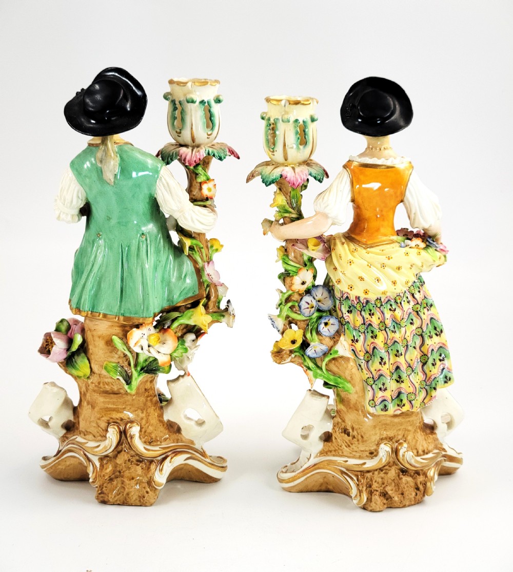 A pair of 18th-century Georgian Derby soft-paste porcelain figural candlesticks depicting a male and female figure in period dress beside candle sconces adorned with colourful flowers and gilt Rococo scrollwork. View IV