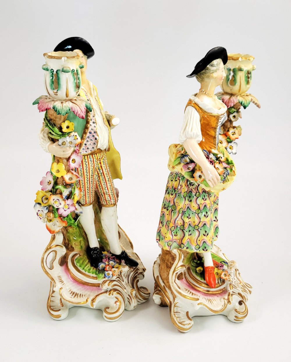 A pair of 18th-century Georgian Derby soft-paste porcelain figural candlesticks depicting a male and female figure in period dress beside candle sconces adorned with colourful flowers and gilt Rococo scrollwork. View VI