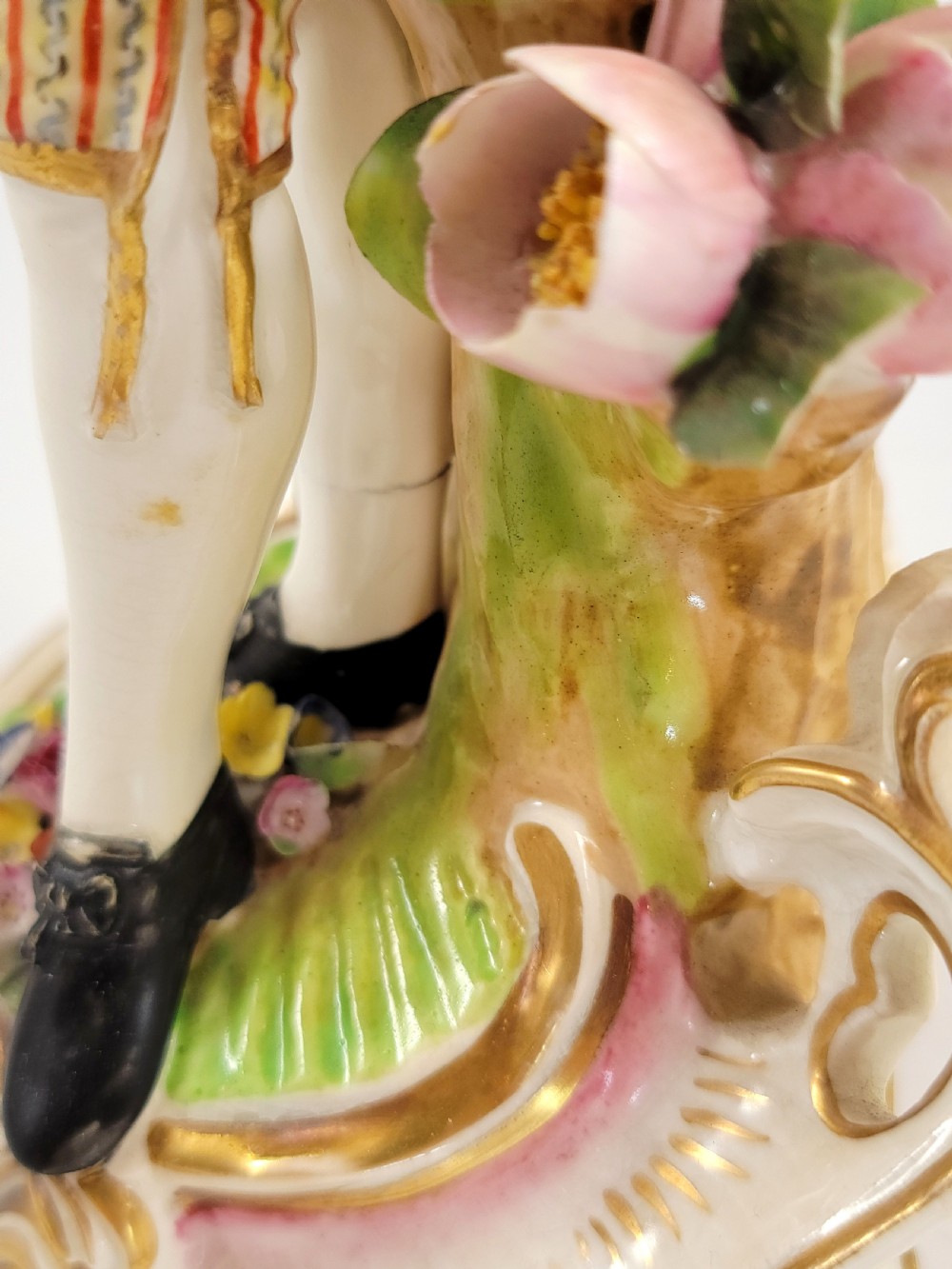 A pair of 18th-century Georgian Derby soft-paste porcelain figural candlesticks depicting a male and female figure in period dress beside candle sconces adorned with colourful flowers and gilt Rococo scrollwork. View IX