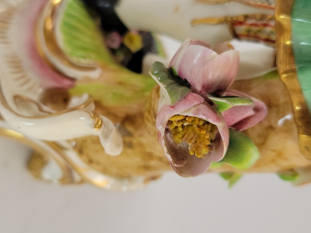 A pair of 18th-century Georgian Derby soft-paste porcelain figural candlesticks depicting a male and female figure in period dress beside candle sconces adorned with colourful flowers and gilt Rococo scrollwork. View X