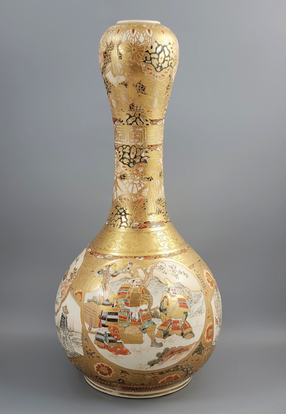 A Japanese Satsuma earthenware vase featuring a bulbous garlic-shaped mouth, intricate gilded borders, and painted panels depicting samurai warriors.