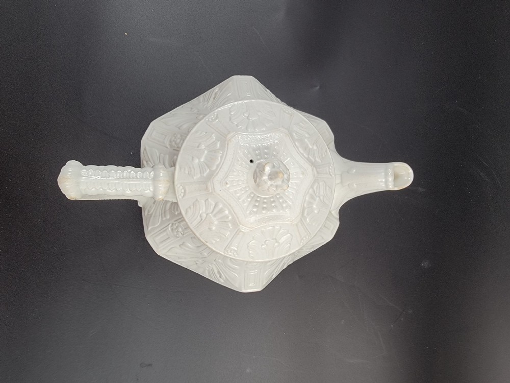 An early 19th-century white stoneware teapot featuring relief-moulded classical foliage, a reeded handle, and a stylized finial. View X