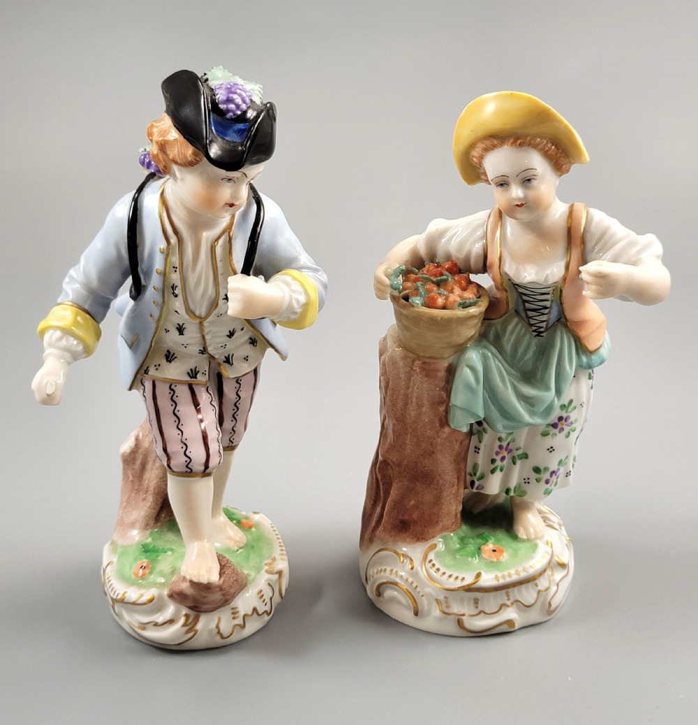 Pair of antique hand-painted Dresden porcelain figurines depicting a boy and girl gathering fruit on gilded Rococo scroll bases.