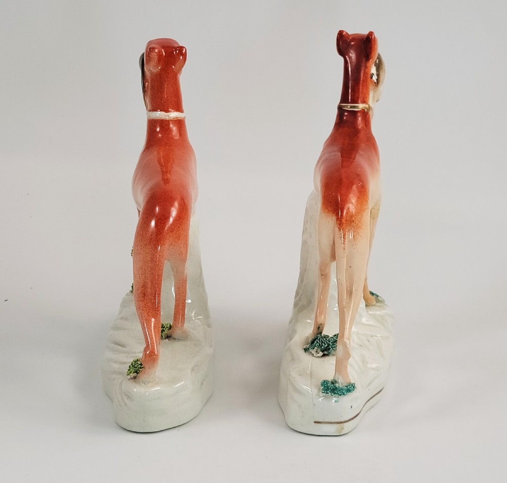 A pair of Victorian Staffordshire earthenware greyhound figurines standing on white bases with caught hares held in their mouths. View III