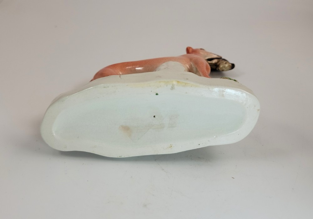 A pair of Victorian Staffordshire earthenware greyhound figurines standing on white bases with caught hares held in their mouths. View VII