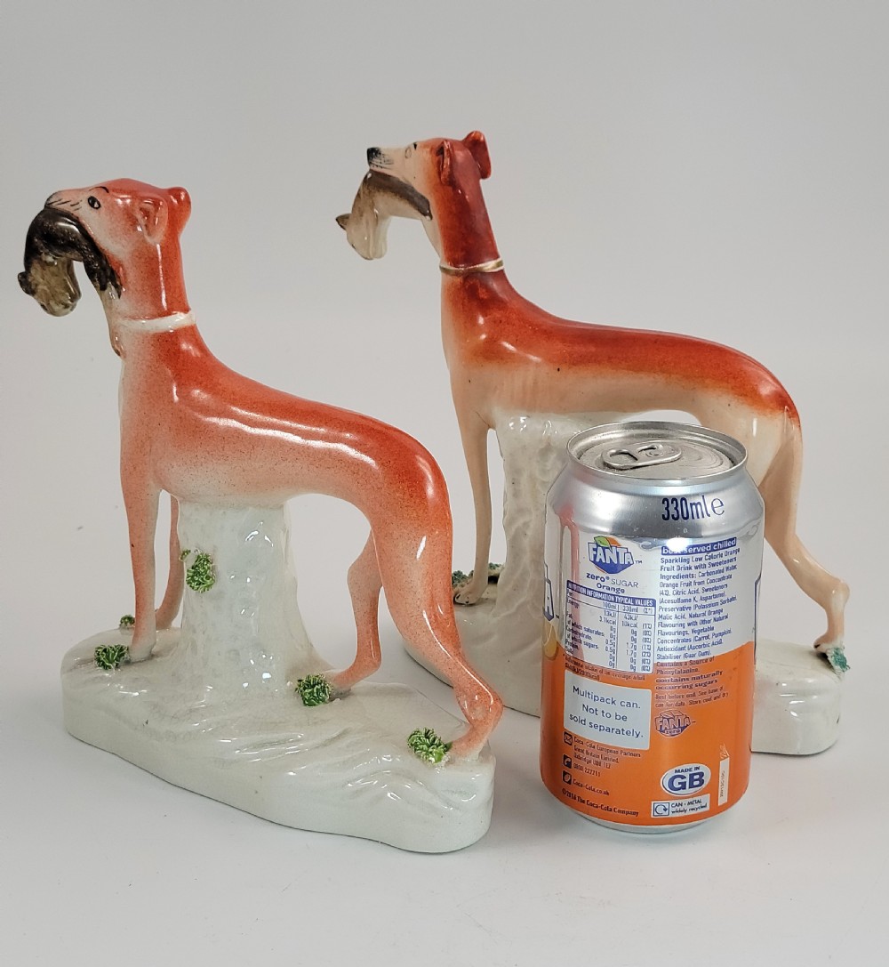 A pair of Victorian Staffordshire earthenware greyhound figurines standing on white bases with caught hares held in their mouths. View XI