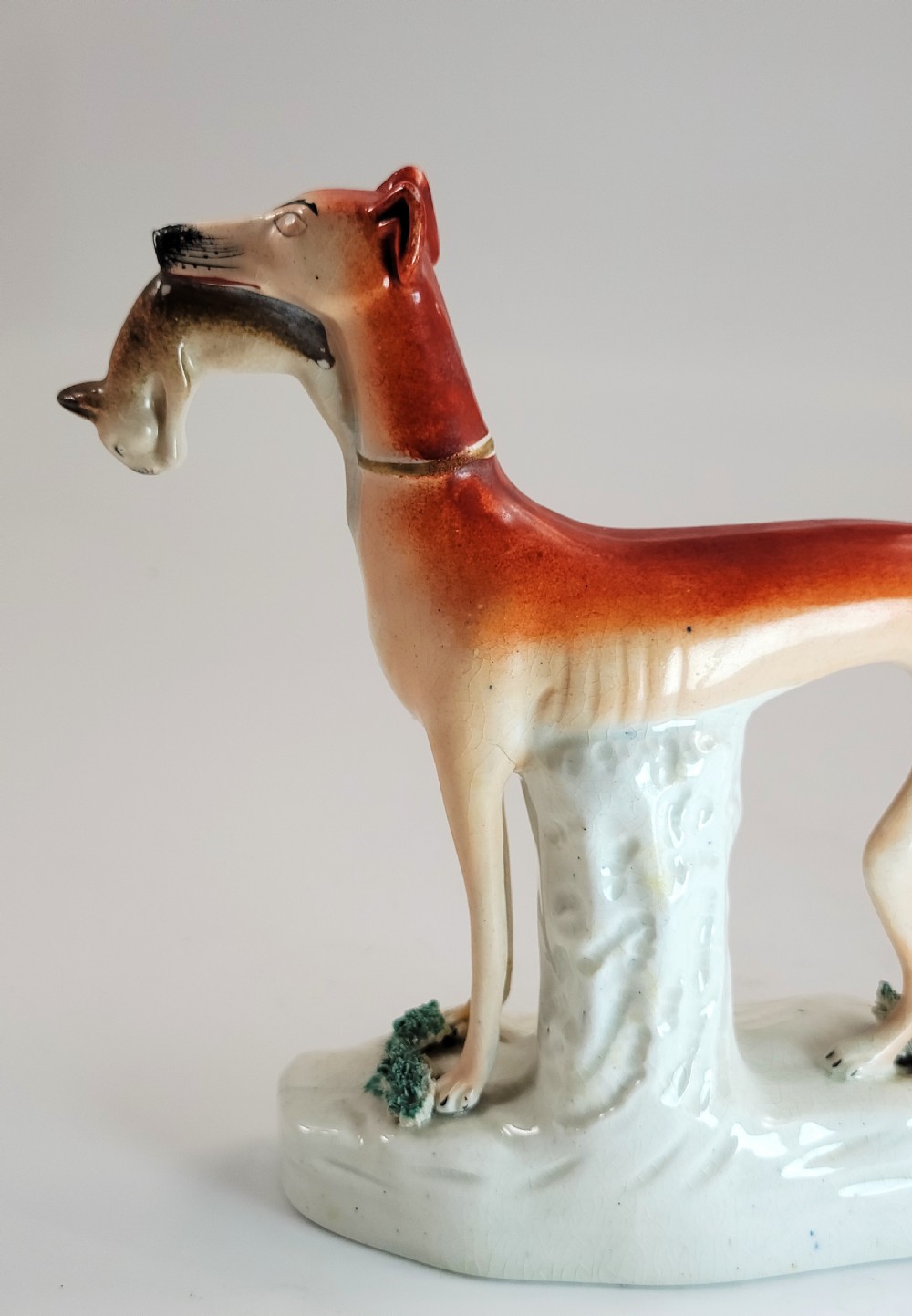 A pair of Victorian Staffordshire earthenware greyhound figurines standing on white bases with caught hares held in their mouths. View XII