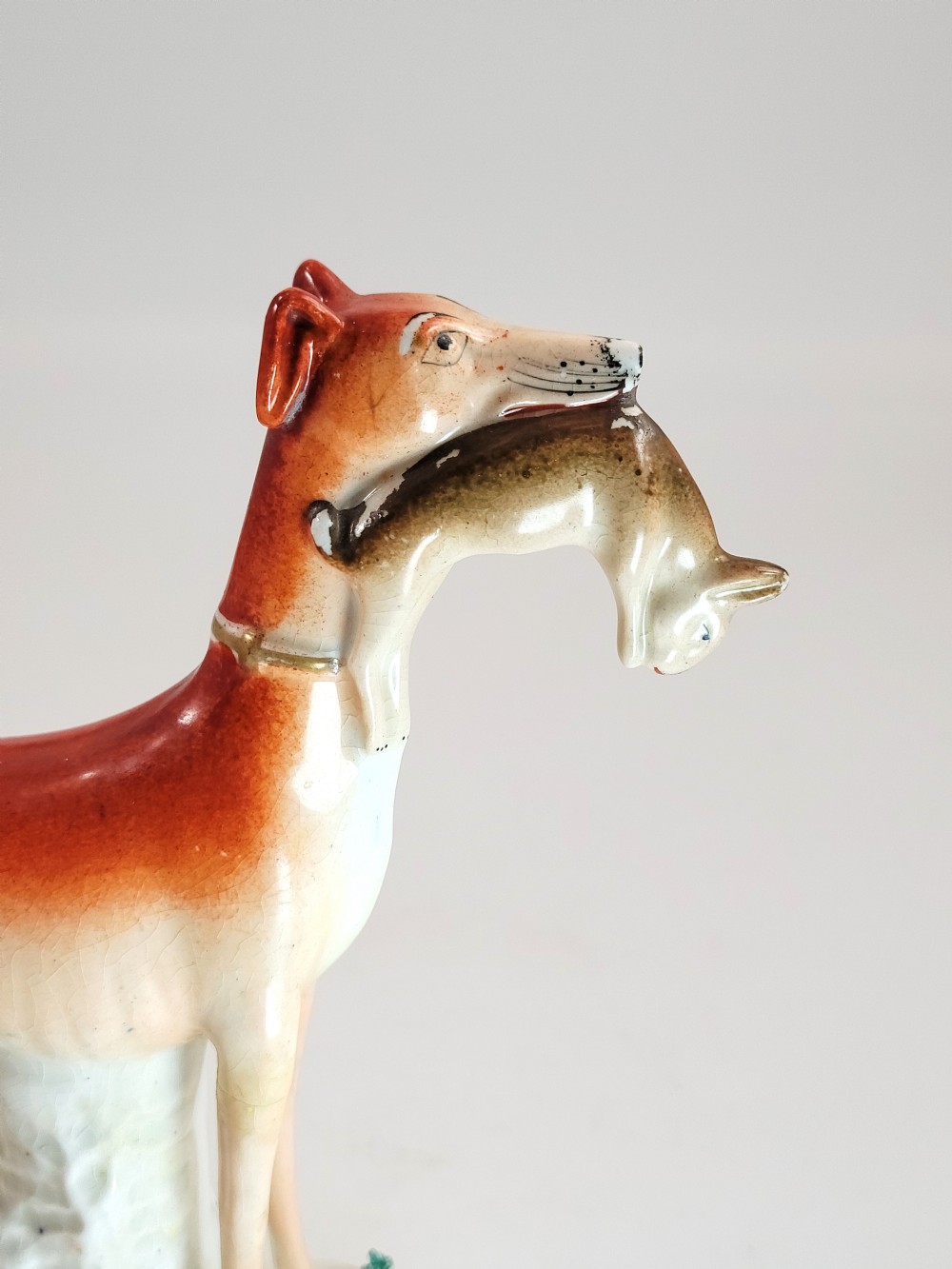 A pair of Victorian Staffordshire earthenware greyhound figurines standing on white bases with caught hares held in their mouths. View XIV