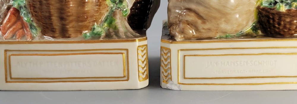 A pair of Royal Copenhagen glazed porcelain figurines depicting a man and woman dressed in traditional Danish Amager market costumes alongside baskets of produce. View XIV