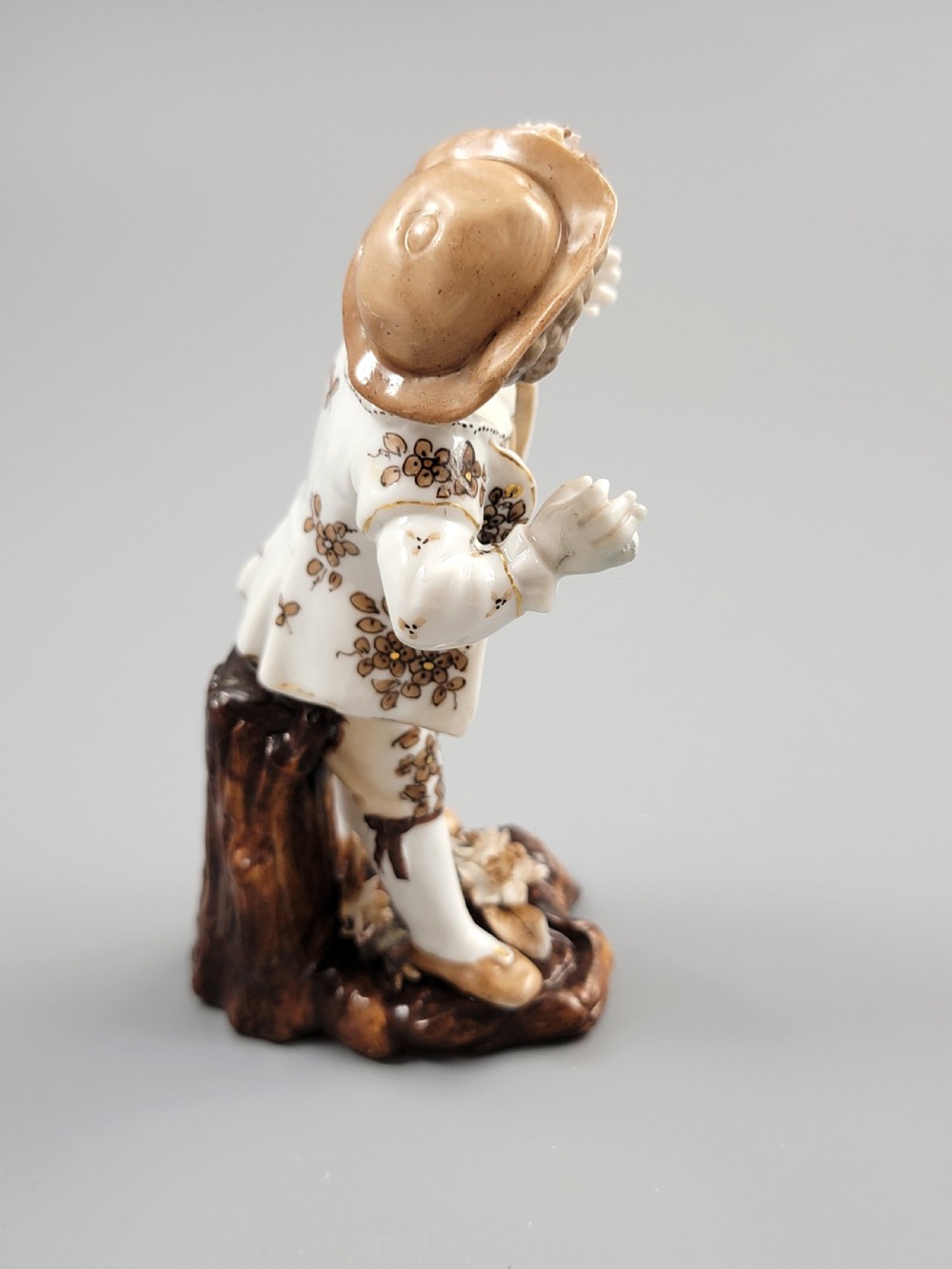 An antique German porcelain figurine depicting a boy wearing a floral coat and holding a small bird on his hand. View V