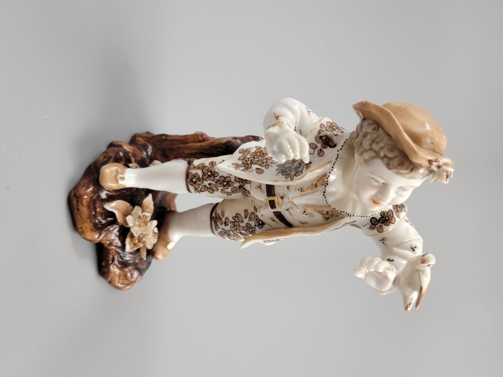 An antique German porcelain figurine depicting a boy wearing a floral coat and holding a small bird on his hand. View VI