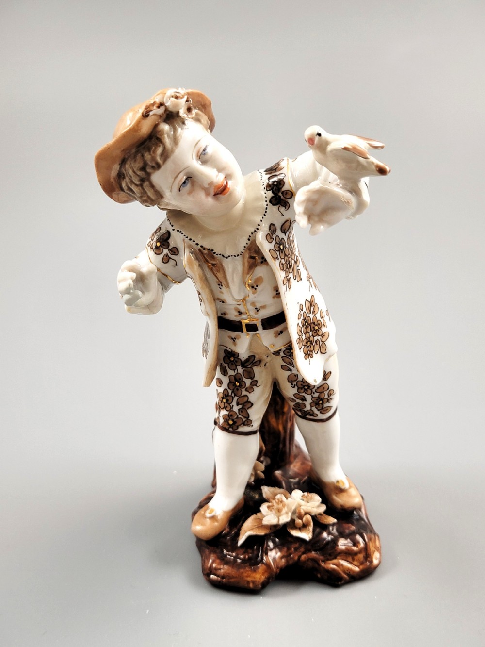An antique German porcelain figurine depicting a boy wearing a floral coat and holding a small bird on his hand. View VII
