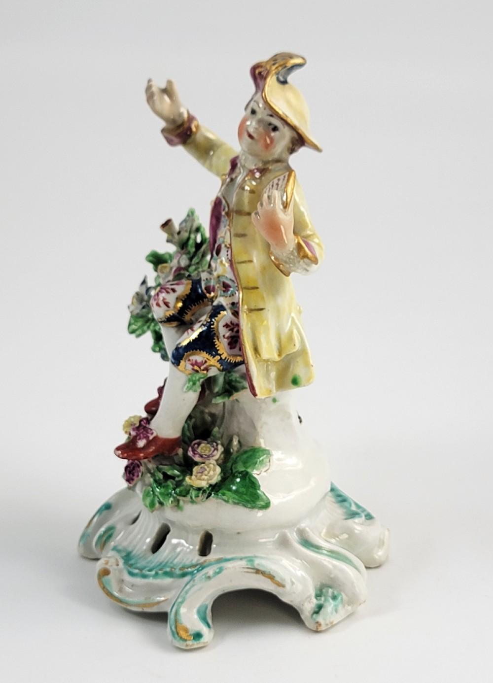 An eighteenth-century Bow soft-paste porcelain figurine depicting a seated boy singer holding sheet music atop a pierced scrollwork rococo base with applied floral bocage. View II