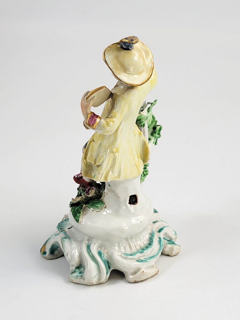 An eighteenth-century Bow soft-paste porcelain figurine depicting a seated boy singer holding sheet music atop a pierced scrollwork rococo base with applied floral bocage. View III