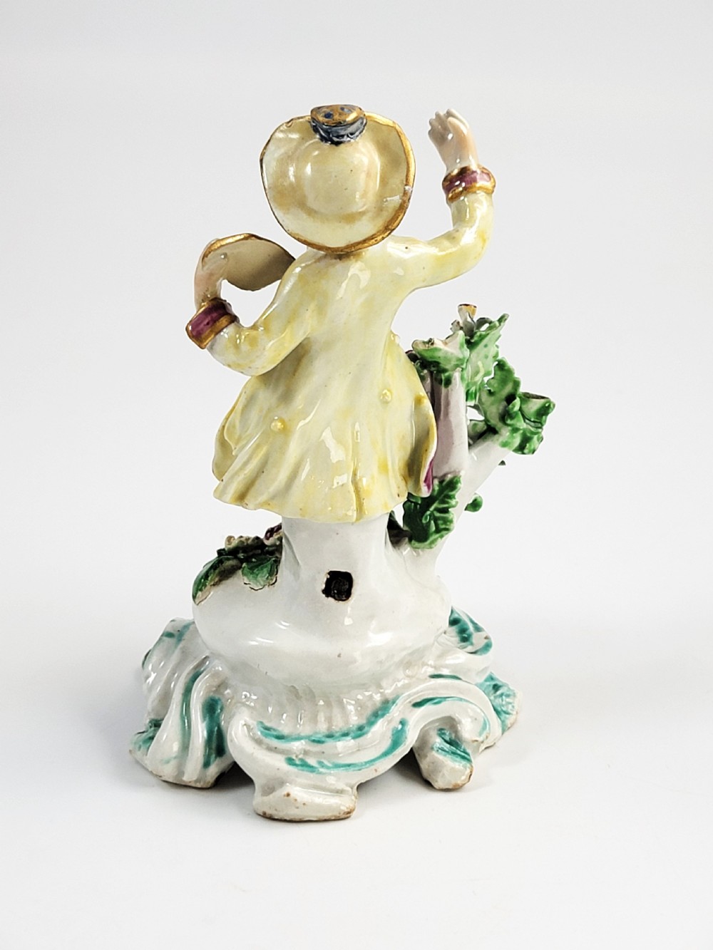 An eighteenth-century Bow soft-paste porcelain figurine depicting a seated boy singer holding sheet music atop a pierced scrollwork rococo base with applied floral bocage. View IV