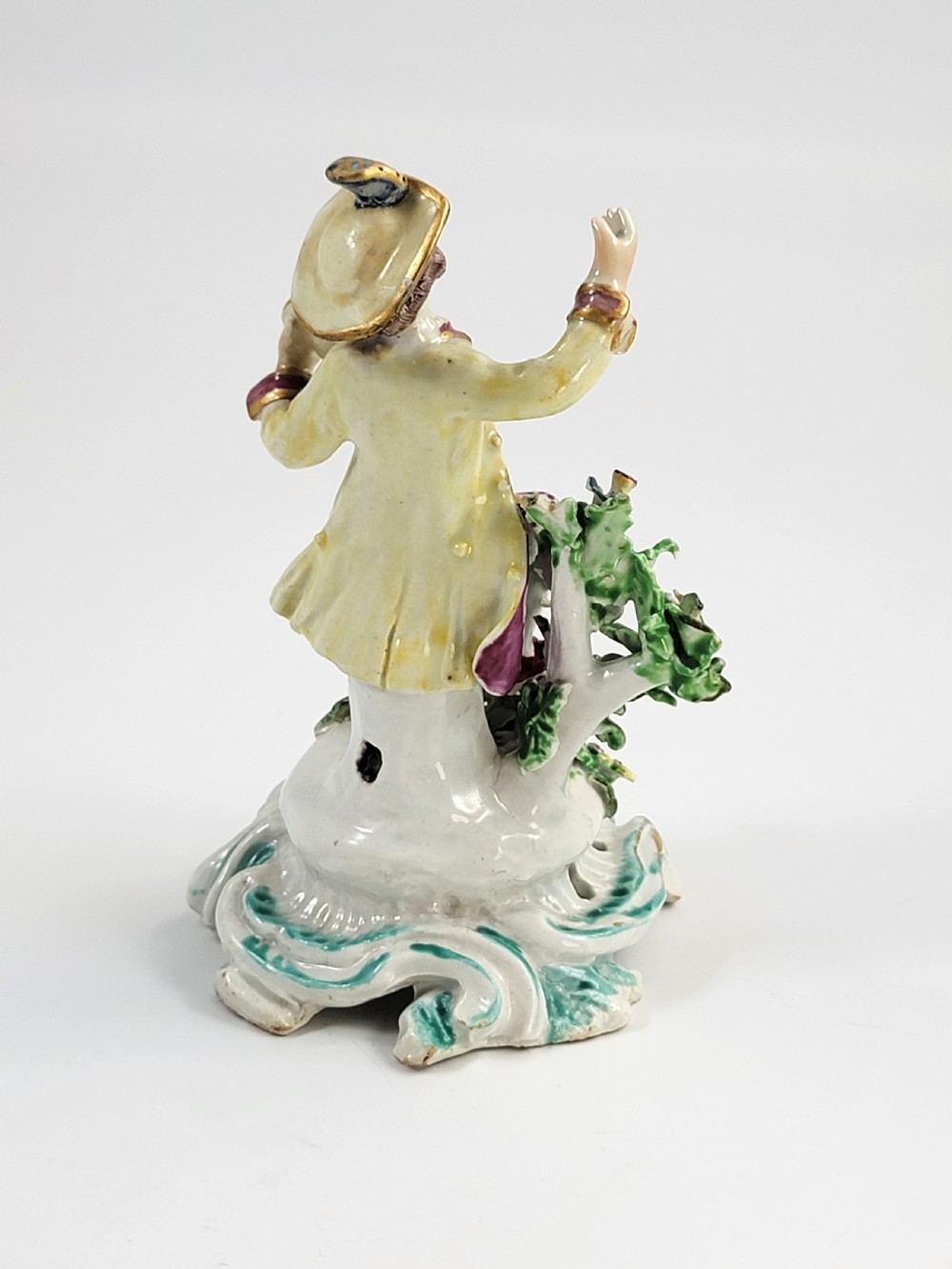 An eighteenth-century Bow soft-paste porcelain figurine depicting a seated boy singer holding sheet music atop a pierced scrollwork rococo base with applied floral bocage. View V