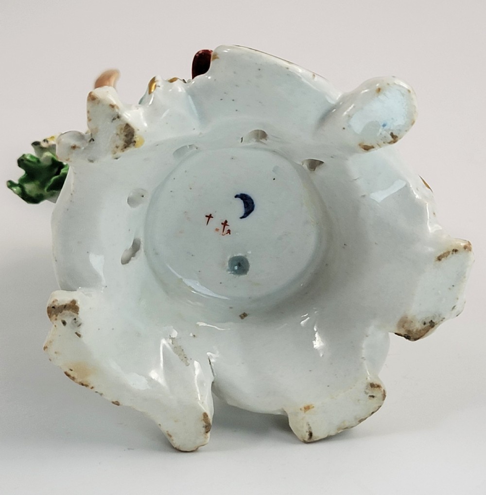 An eighteenth-century Bow soft-paste porcelain figurine depicting a seated boy singer holding sheet music atop a pierced scrollwork rococo base with applied floral bocage. View IX