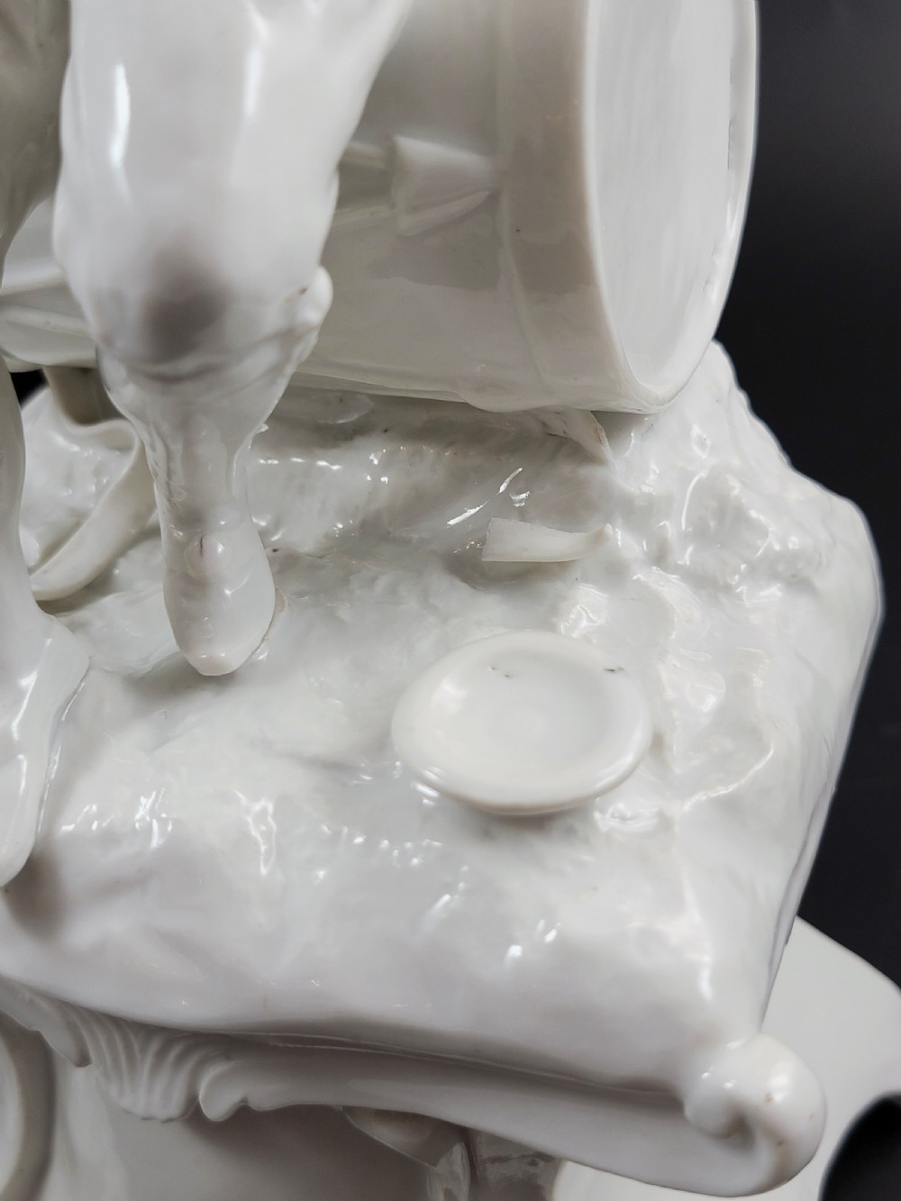 An 18th-century monochrome white glazed porcelain figurine of a male figure seated on a drum atop a Rococo scrollwork base. View VII