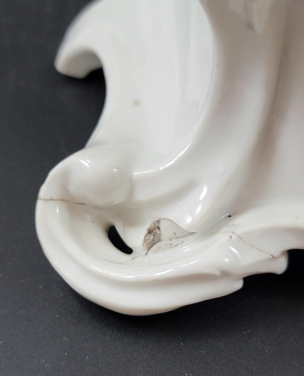 An 18th-century monochrome white glazed porcelain figurine of a male figure seated on a drum atop a Rococo scrollwork base. View X