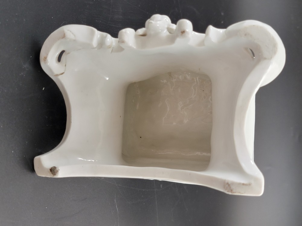 An 18th-century monochrome white glazed porcelain figurine of a male figure seated on a drum atop a Rococo scrollwork base. View XI