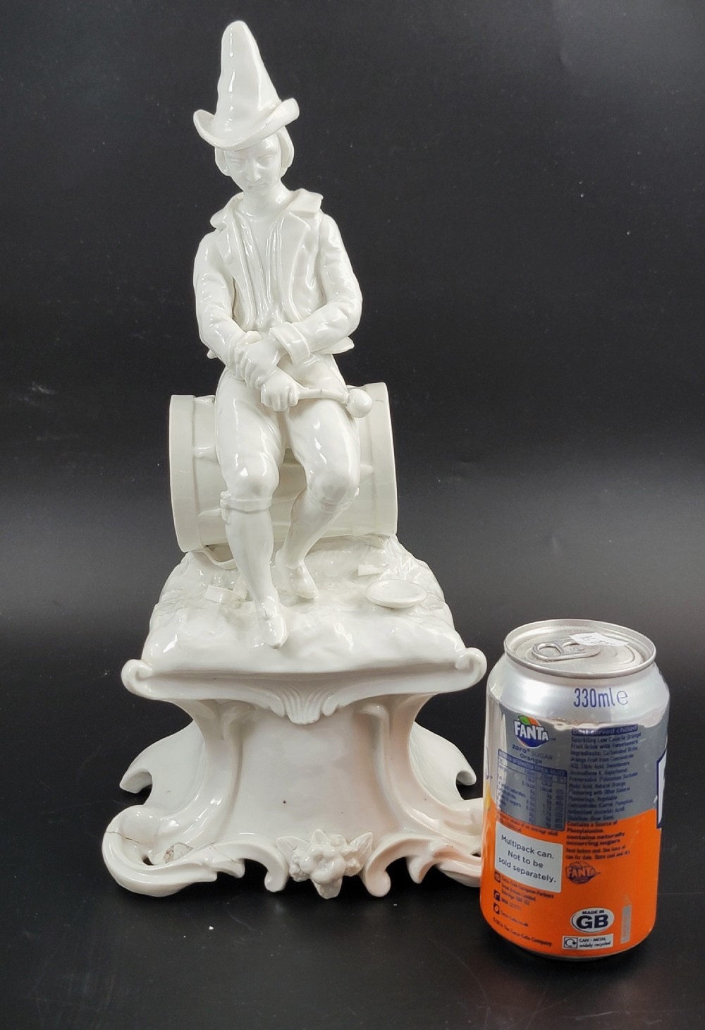 An 18th-century monochrome white glazed porcelain figurine of a male figure seated on a drum atop a Rococo scrollwork base. View XII