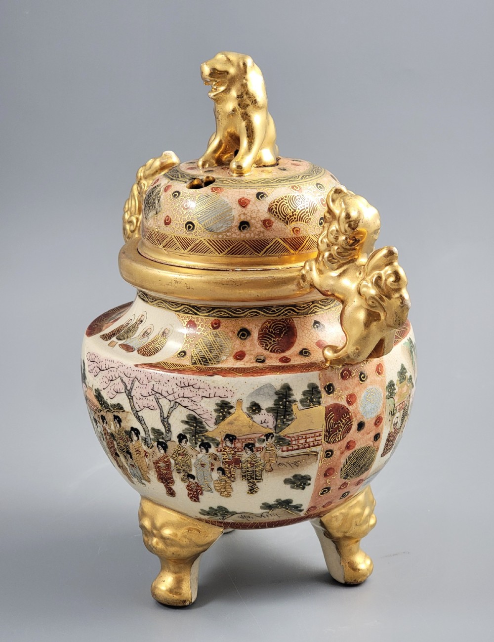 A Japanese Meiji period Satsuma earthenware incense burner featuring gilt shishi handles and finial with detailed hand-painted figures over a crackle glaze. View II
