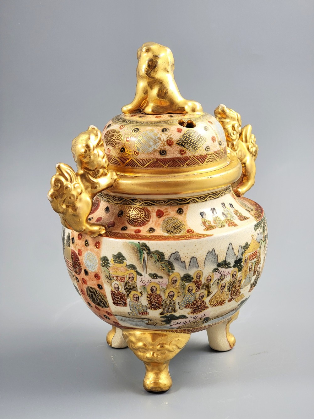 A Japanese Meiji period Satsuma earthenware incense burner featuring gilt shishi handles and finial with detailed hand-painted figures over a crackle glaze. View III