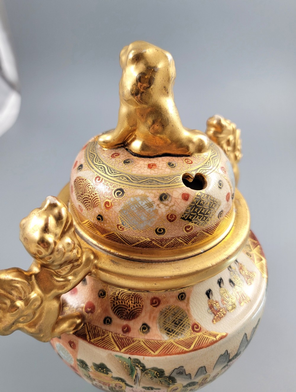 A Japanese Meiji period Satsuma earthenware incense burner featuring gilt shishi handles and finial with detailed hand-painted figures over a crackle glaze. View XIII