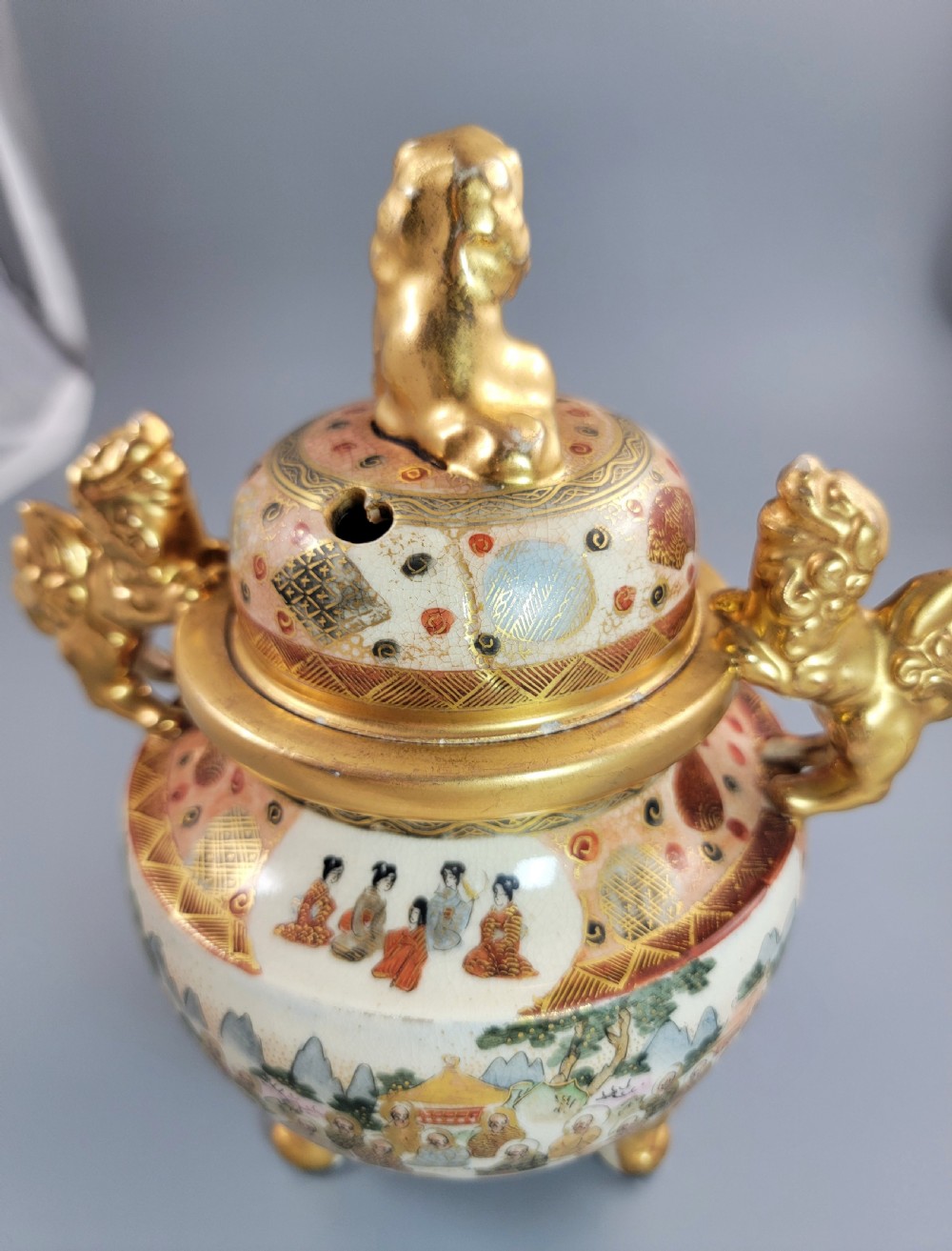 A Japanese Meiji period Satsuma earthenware incense burner featuring gilt shishi handles and finial with detailed hand-painted figures over a crackle glaze. View XV