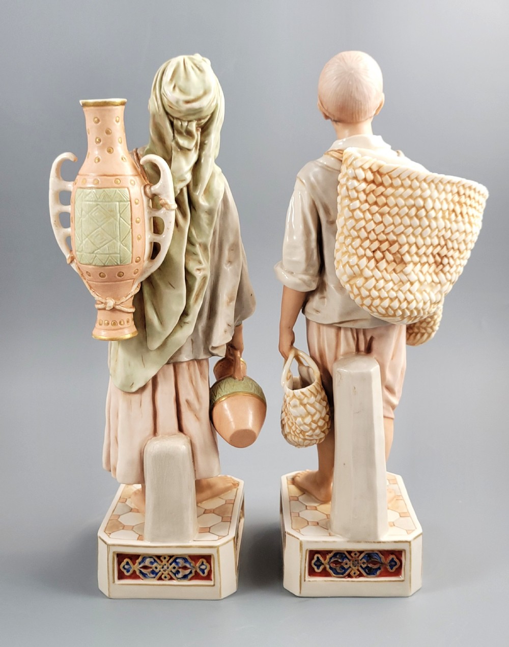 A pair of late 19th-century Royal Dux porcelain figurines depicting a male and female water bearer in draped attire standing on patterned pedestal bases. View III