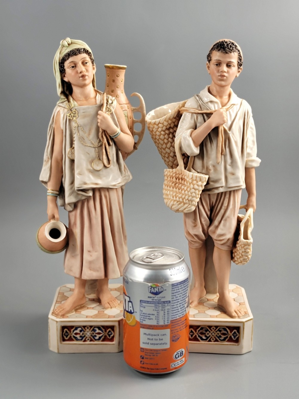 A pair of late 19th-century Royal Dux porcelain figurines depicting a male and female water bearer in draped attire standing on patterned pedestal bases. View VIII