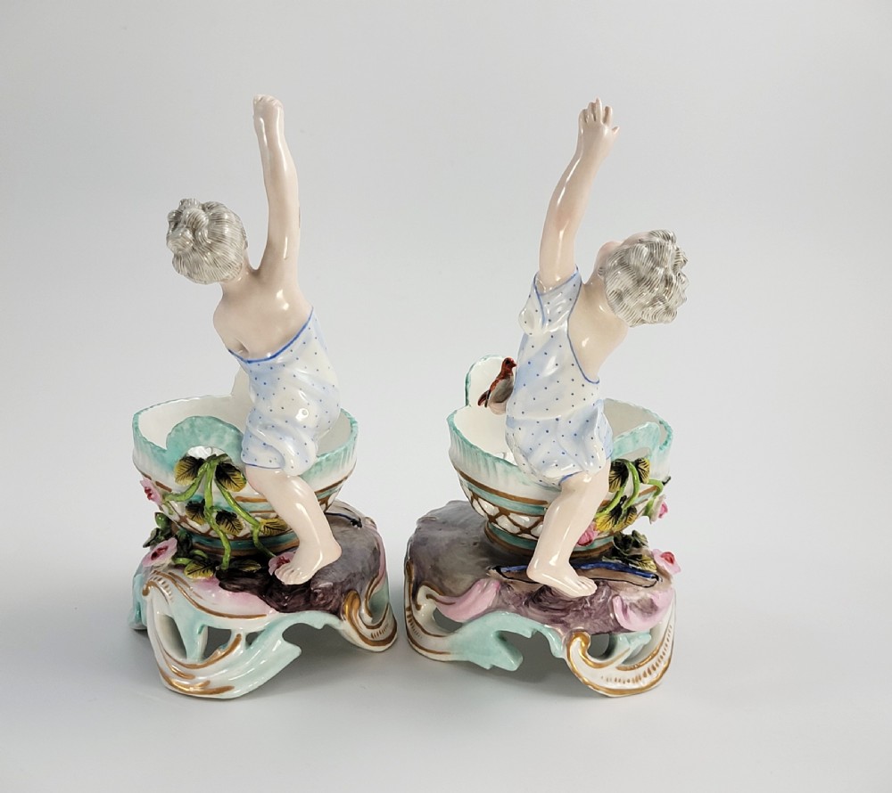 A pair of 19th-century German porcelain sweetmeat figures featuring sculpted children with birds beside reticulated baskets on ornate scrollwork bases. View III