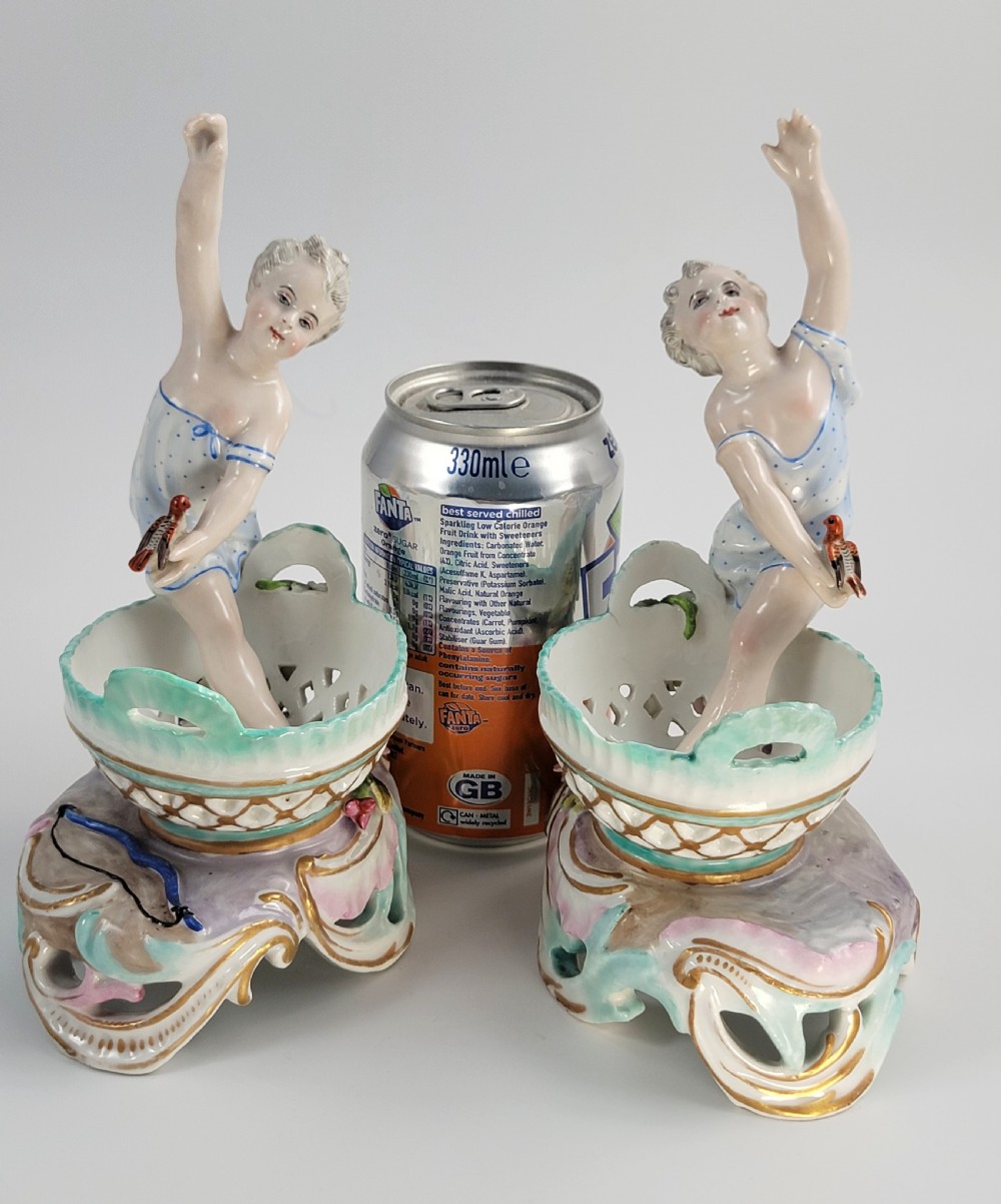 A pair of 19th-century German porcelain sweetmeat figures featuring sculpted children with birds beside reticulated baskets on ornate scrollwork bases. View XIII