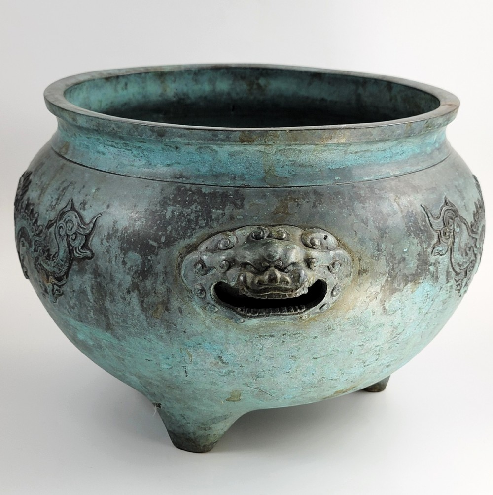 A tripod Chinese bronze censer decorated with raised dragon motifs, mask handles, and a verdigris surface finish. View III