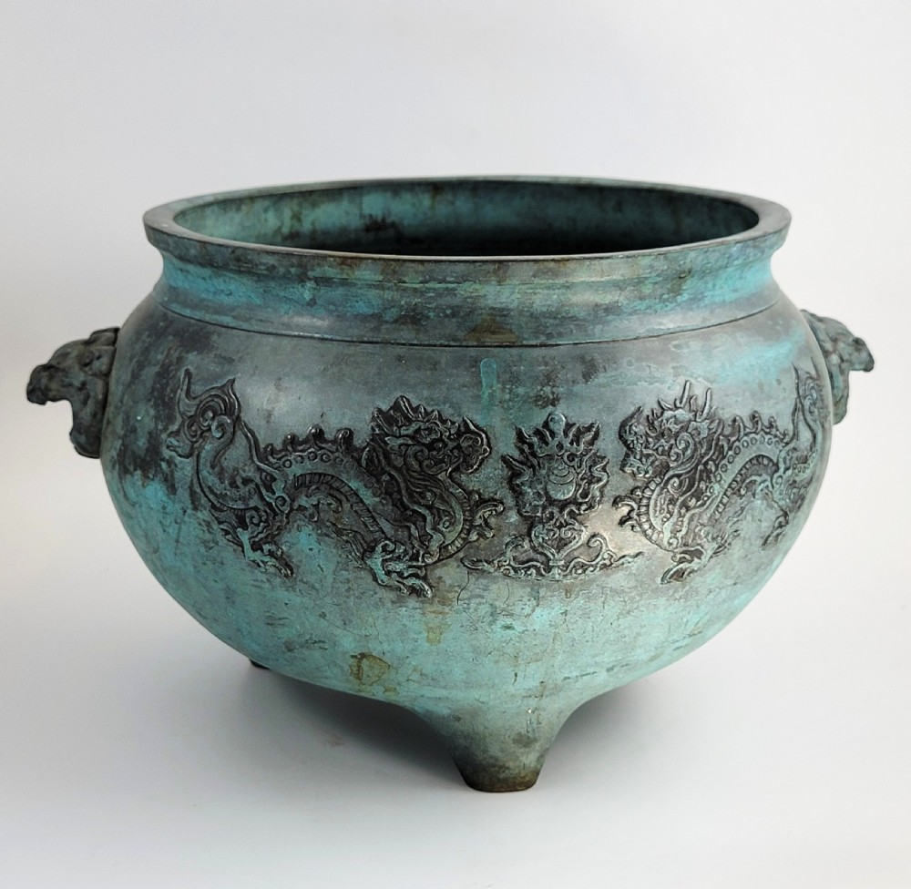 A tripod Chinese bronze censer decorated with raised dragon motifs, mask handles, and a verdigris surface finish. View IV