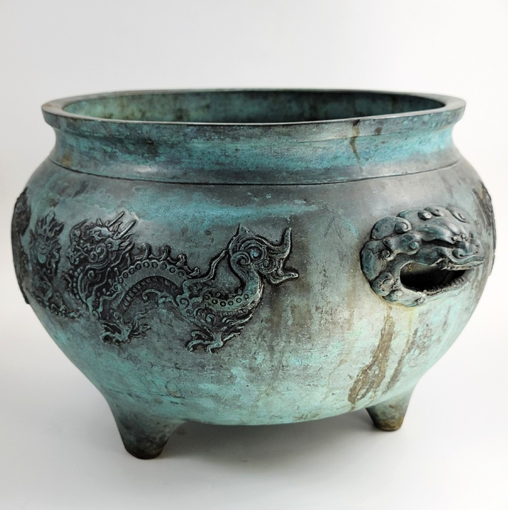 A tripod Chinese bronze censer decorated with raised dragon motifs, mask handles, and a verdigris surface finish. View VI