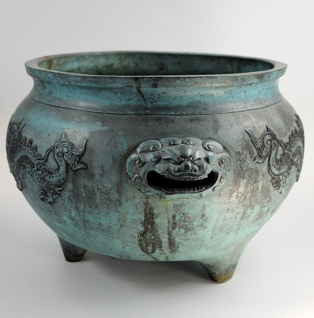 A tripod Chinese bronze censer decorated with raised dragon motifs, mask handles, and a verdigris surface finish. View VII