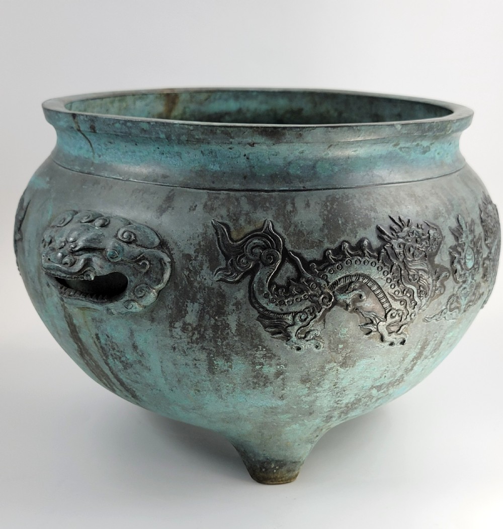 A tripod Chinese bronze censer decorated with raised dragon motifs, mask handles, and a verdigris surface finish. View VIII