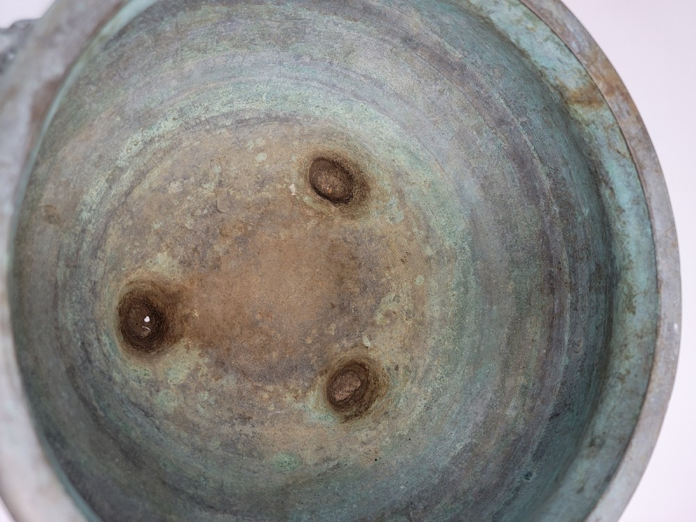 A tripod Chinese bronze censer decorated with raised dragon motifs, mask handles, and a verdigris surface finish. View XII